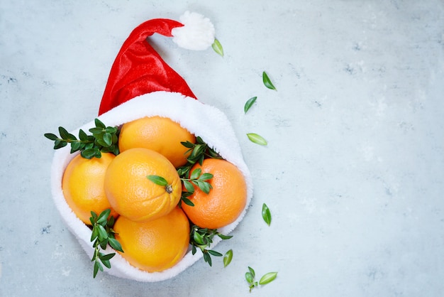 Rijpe sinaasappelen in de hoed van Santa Claus met bukshoutinstallatie op een blauwe achtergrond