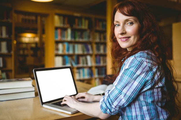 Rijpe student die in bibliotheek met laptop bestudeert