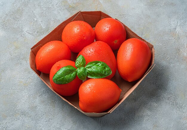 Rijpe tomaten en basilicum in milieuvriendelijke verpakking op een grijze muur. Zijaanzicht, close-up.