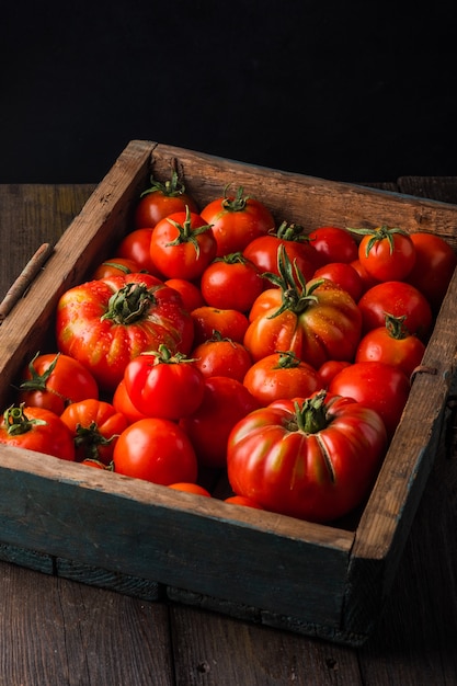 Rijpe tomaten in een houten kist Verse groenten op een zwarte houten achtergrond