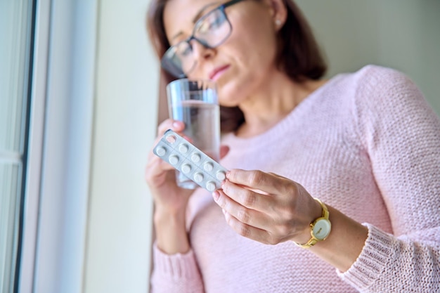 Rijpe trieste vrouw met blister van pillen en glas water thuis