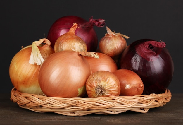 Rijpe uien op rieten wieg op houten tafel op zwarte achtergrond