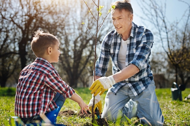 Rijpe vader die zoontje leert hoe hij voor de natuur moet zorgen door een boom in de tuin van een landhuis te zetten