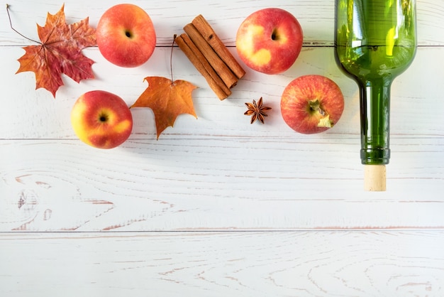 Rijpe verse, sappige rode appels, kruiden, fles op een lichte houten ondergrond met herfstbladeren.