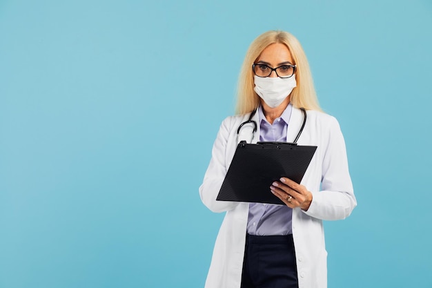 Rijpe vrouw arts in masker houdt map op blauwe achtergrond. Covid-19-concept