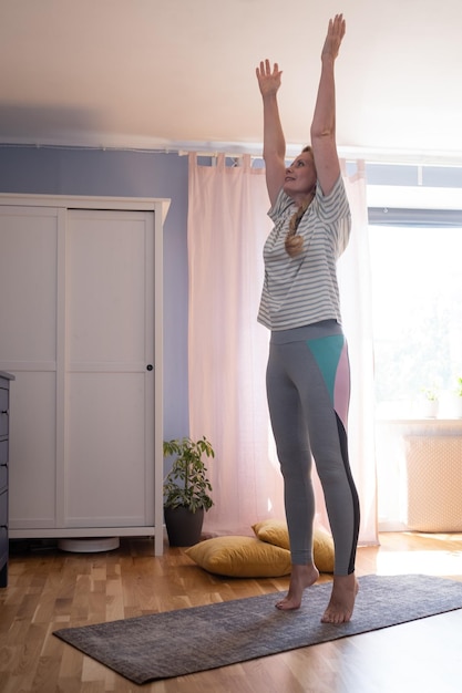 Rijpe vrouw die binnenshuis traint terwijl ze in de tadasana-berghouding staat