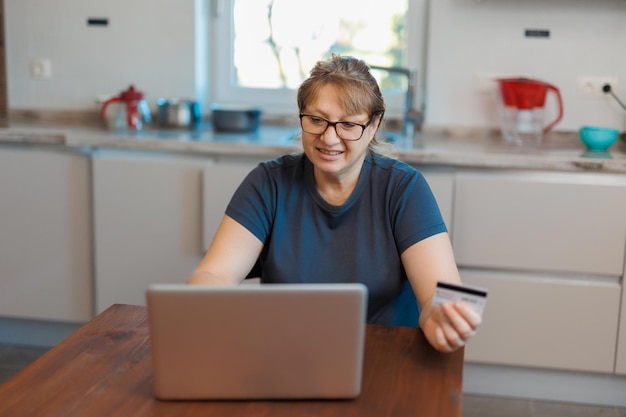 Rijpe vrouw die een creditcard gebruikt en thuis online betaalt