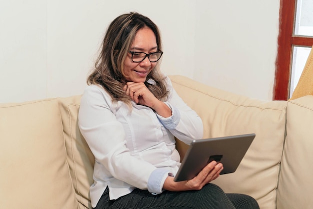 Rijpe vrouw die een digitale tablet gebruikt terwijl ze thuis papierwerk doet