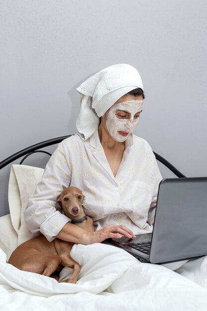 Rijpe vrouw die haar gezicht met een gezichtsmasker in bed met hond behandelen