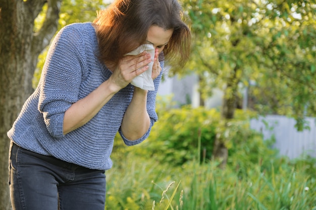 Rijpe vrouw die in zakdoek niest, allergie voor stuifmeel, verkoudheid