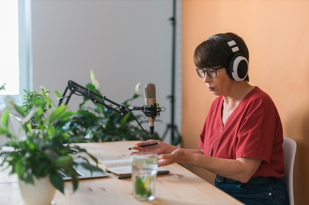 Rijpe vrouw die podcastopname maakt voor haar online show Aantrekkelijke zakenvrouw die een koptelefoon voor de microfoon gebruikt voor een radio-uitzending