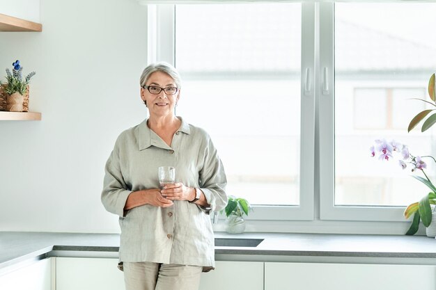 Rijpe vrouw drinkt schoon water terwijl ze in de keuken staat