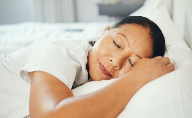 Rijpe vrouw en kalm tijdens het slapen in bed met goede droom hoofd op kussen en vrede Aziatische bejaarde en gezicht in de slaapkamer alleen en glimlach van geluk terwijl rust met pensioen in huis