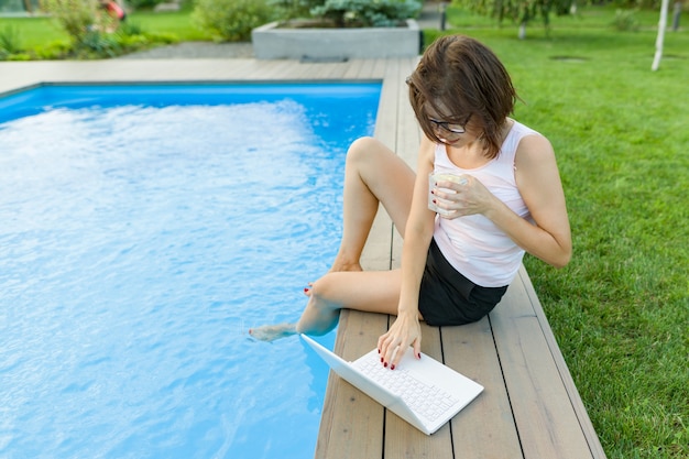 Rijpe vrouw freelancer gebruikt aptop bij het zwembad