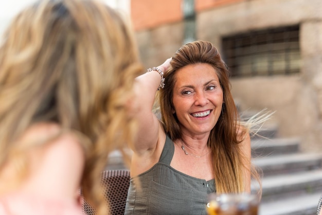 Foto rijpe vrouw in een café met een drankje met haar vrienden. vrouw van middelbare leeftijd die lacht en haar hand op haar haar legt.