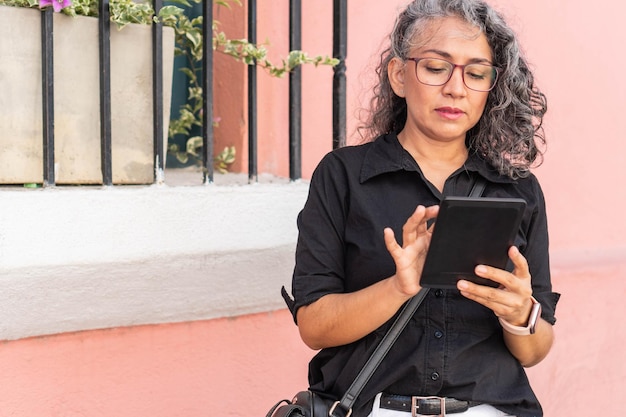 Rijpe vrouw in glazen houdt tablet buitenshuis