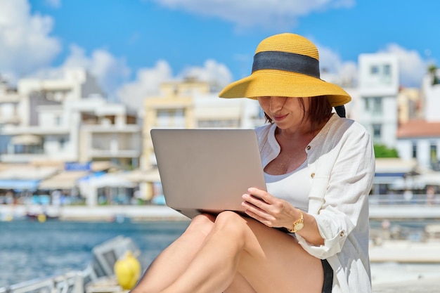 Rijpe vrouw in hoed met laptop op de boulevard in de stad