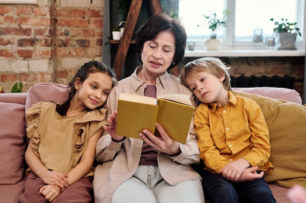 Rijpe vrouw leesboek met haar kleinkinderen in de woonkamer