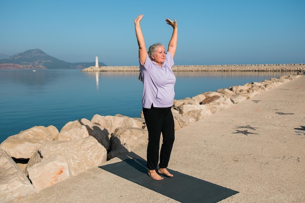 Rijpe vrouw met dreadlocks die yoga-oefeningen doen op het welzijn van het zeestrand en ac