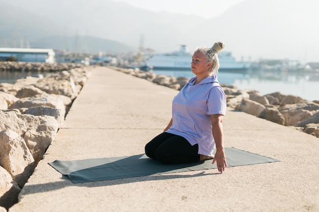 Rijpe vrouw met dreadlocks die yoga-oefeningen doen op het welzijn van het zeestrand en het concept van actieve ouderen