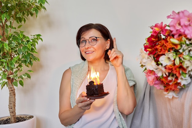 Rijpe vrouw met kleine verjaardagstaart met brandende kaarsen