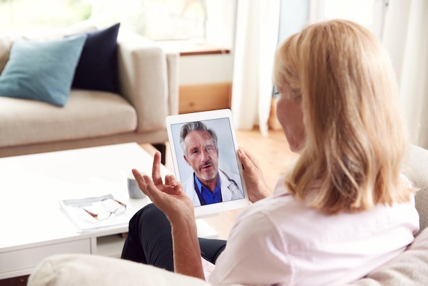 Rijpe vrouw met online overleg met arts thuis op digitale Tablet