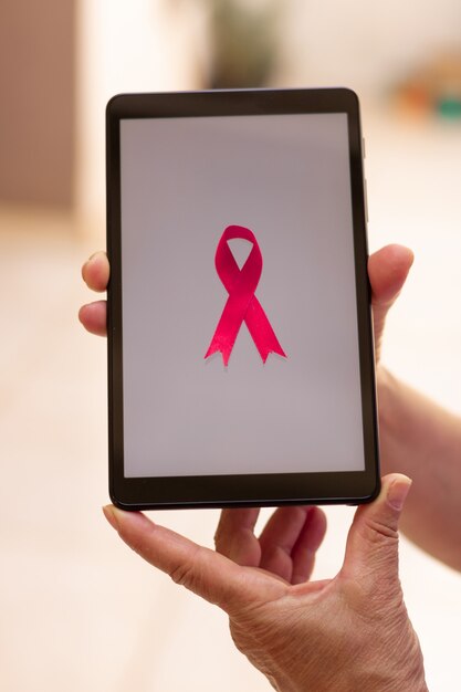 Rijpe vrouw met tablet met een roze lint. Breast Cancer Awareness Month met tech afbeelding.