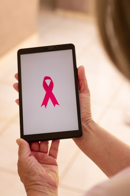 Rijpe vrouw met tablet met een roze lint. Breast Cancer Awareness Month met tech afbeelding.