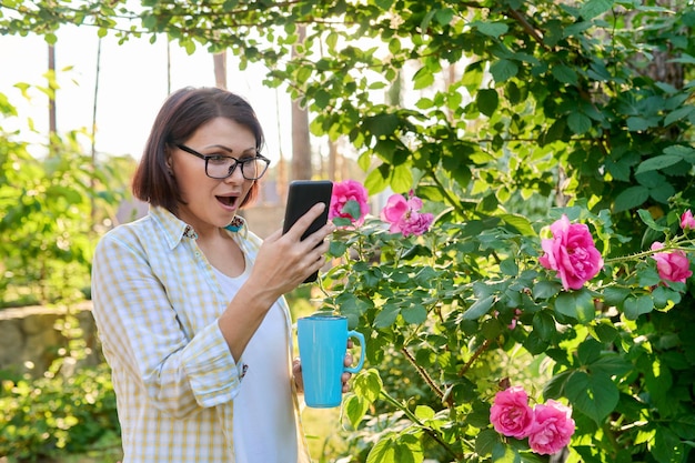 Rijpe vrouw rustend in de achtertuin met behulp van smartphone voor video-oproep