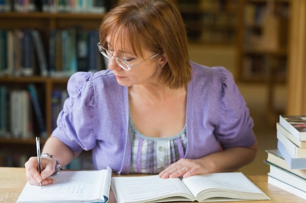 Rijpe vrouwelijke student het schrijven nota&#39;s bij bureau in de bibliotheek