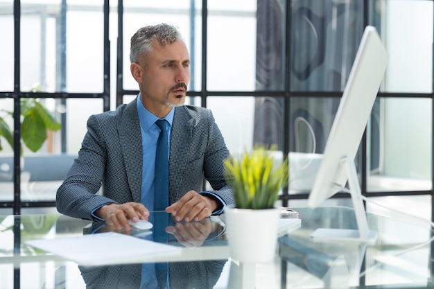 Rijpe zakenman die aan computer in modern bureau werkt