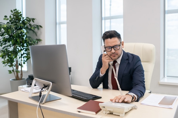 Rijpe zakenman die telefoonnummer kiest op zijn werkplek