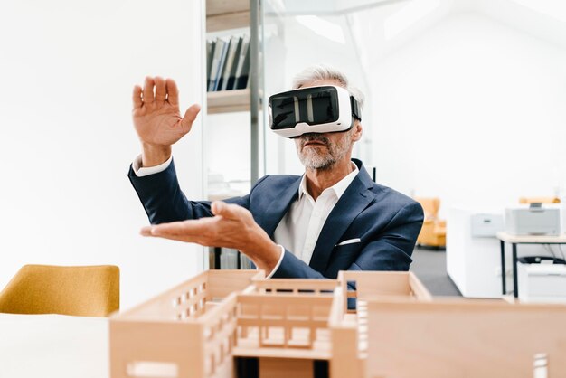 Rijpe zakenman met architectonisch model in kantoor met een VR-bril