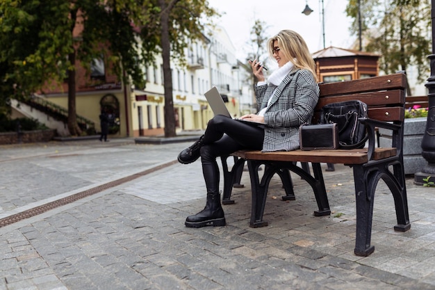 Rijpe zakenvrouw in het park op een bankje met een laptop op haar knieën spreekt via videoverbinding