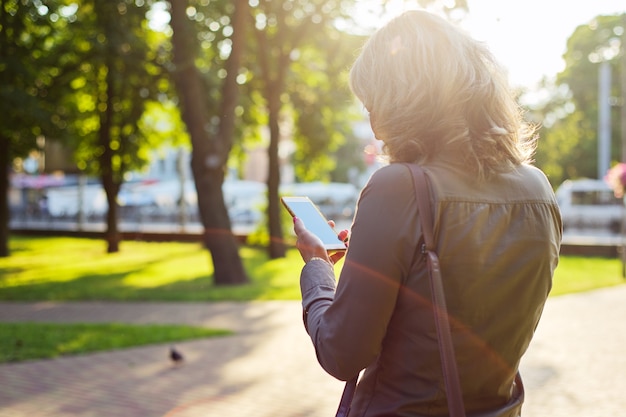 Rijpe zakenvrouw met smartphone. Zonnige dag op de achtergrond van de stad.