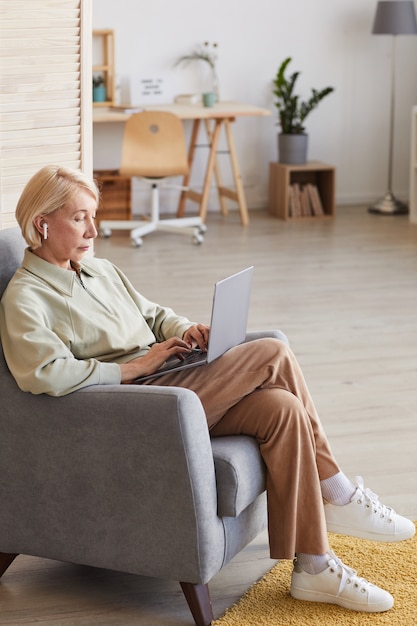 Rijpe zakenvrouw zittend op een stoel en een bericht typen op haar laptopcomputer in de kamer