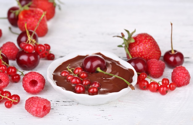 Rijpe zoete bessen en vloeibare chocolade op houten tafel