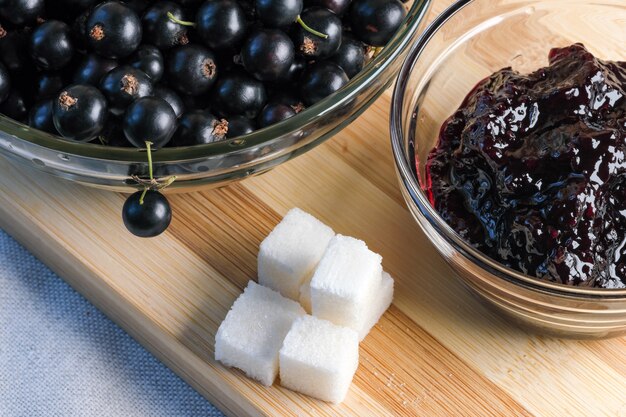 Rijpe zwarte bessen op de keukentafel naast een kom aalbessenjam en suikerklontjes close-up macrofotografie