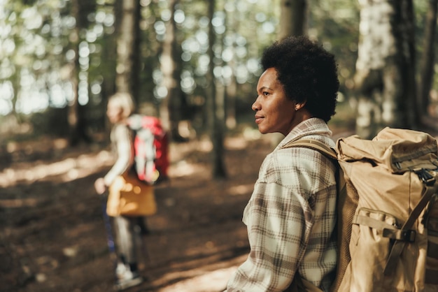 Rijpe zwarte vrouw met rugzak wandelen door het bos.