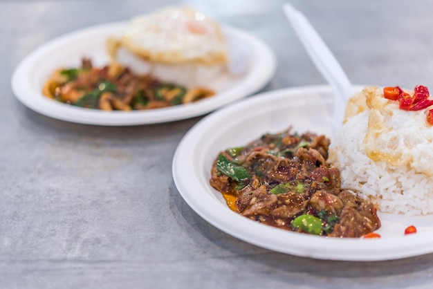 Rijst bedekt met geroerbakte varkensvlees of rundvlees en basilicum te koop bij Thaise straatvoedsel markt of restaurant