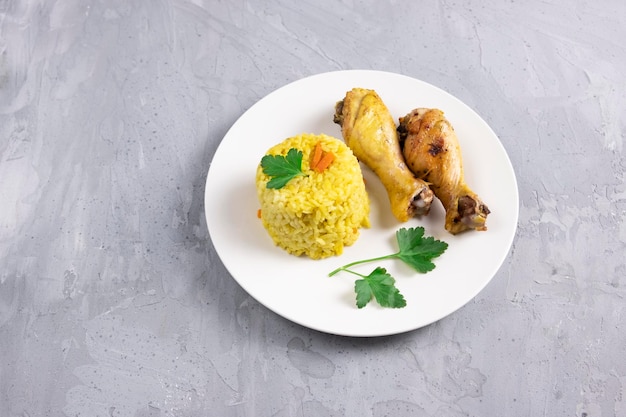 Rijst met kurkuma en gebakken kippenpoten op witte plaat op een grijze achtergrond