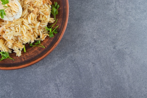 Rijst met vermicelli op een bord naast groenten, op de blauwe achtergrond.