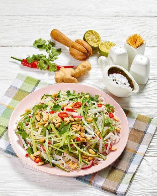 Rijstnoedels en groentesalade op een bord op een houten tafel met dressing in een juskom, aziatische keuken, horizontale weergave van bovenaf