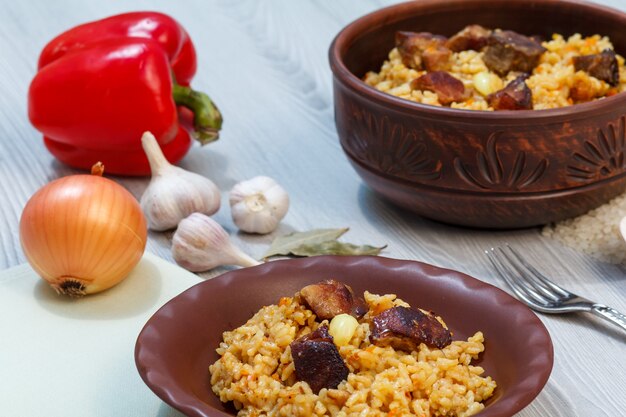 Rijstpilaf op kleiplaat en kom met vlees en groenten - ui, knoflook, rode peper, paprika