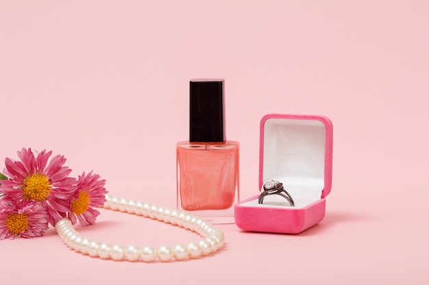 상자에 반지, 매니큐어, 분홍색 배경의 끈에 있는 구슬. 여성용 보석, 화장품 및 액세서리.