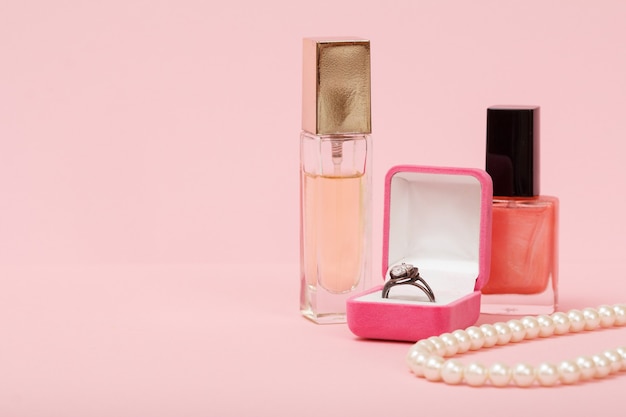 Ring in a box, nail polish, perfume and beads on a pink background. Women jewelry, cosmetics and accessories.