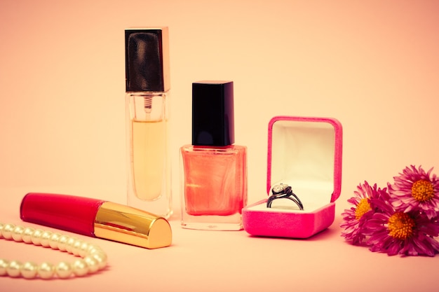 Ring in a box, nail polish, perfume, lipstick, beads and flowers on a pink background. Women jewelry, cosmetics and accessories. Color toned.