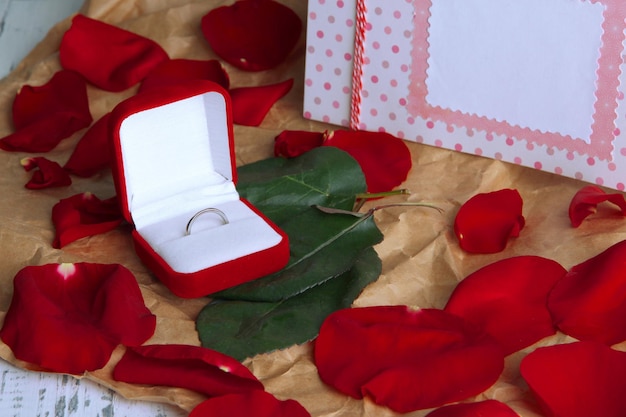 Ring surrounded by roses and petals on wooden table close-up