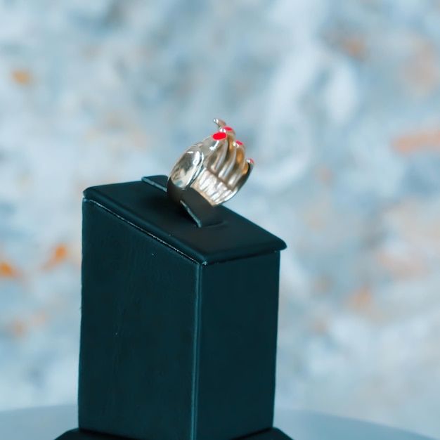 A ring with a red heart on it sits on a black box.