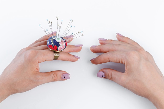 A ring with a small pillow for needles on a hand and scissors on a white background